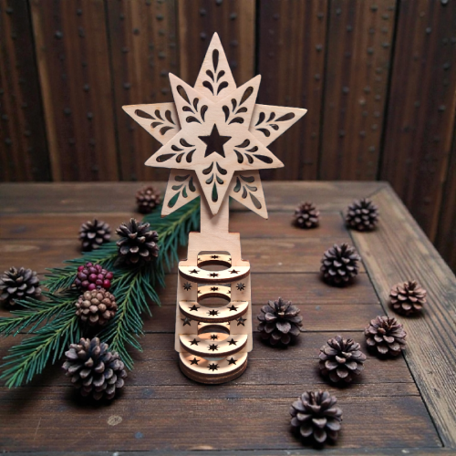 Drewniany czubek na choinkę w formie ażurowej gwiazdy ze sklejki, ustawiony na świątecznym tle z szyszkami.webp